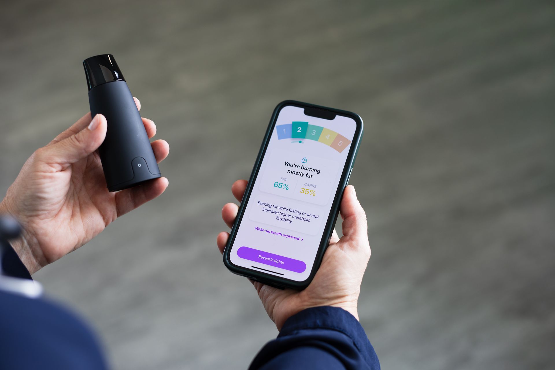 Person holding a black device and a smartphone displaying data with colored segments.