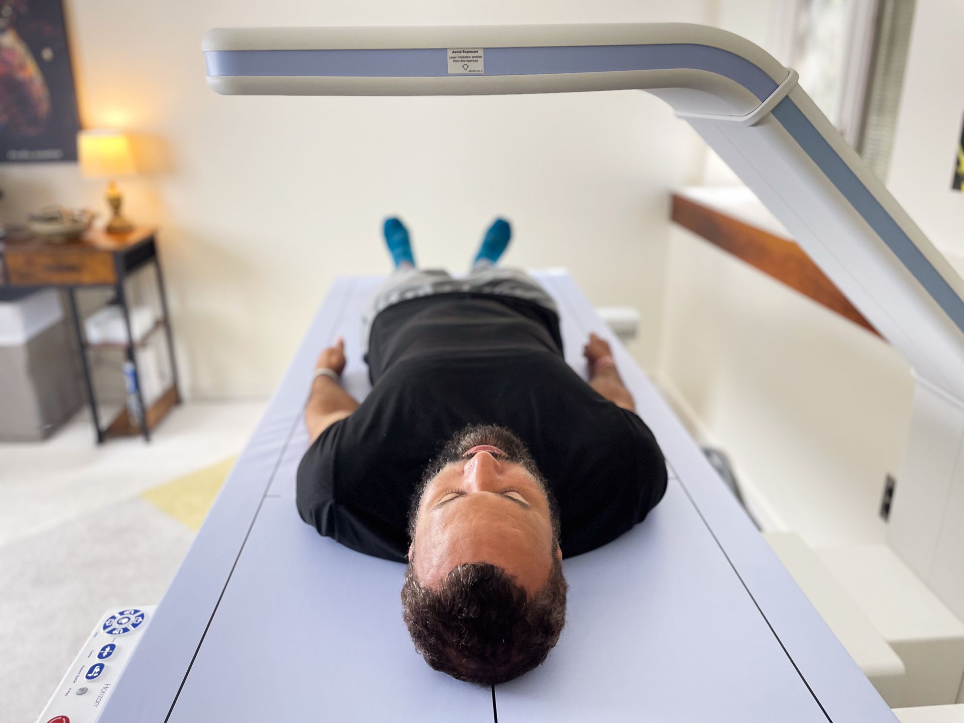 Man lying on a white scanner bed under a light, indoors.