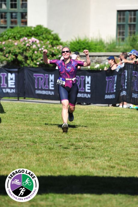 Runner in a purple jersey celebrates on a grassy finish area at an outdoor race.