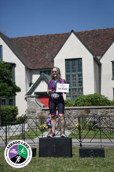 Person standing on a podium holding a sign, in front of a building with a red roof and stone wall.