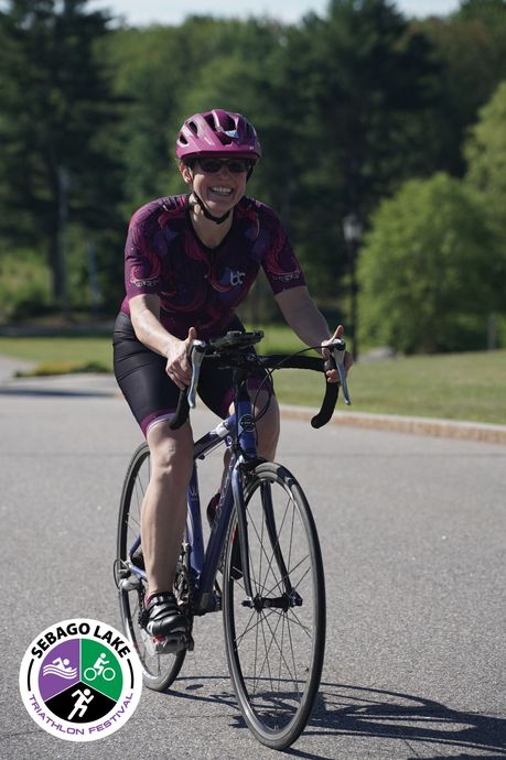Cyclist in purple jersey and helmet riding on a sunny road near trees