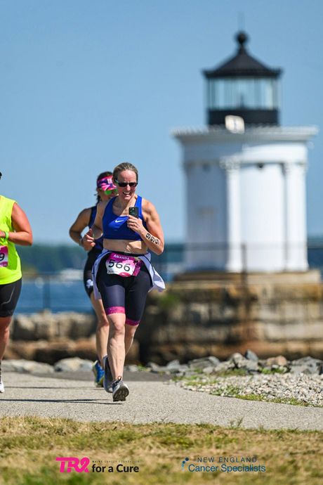 Runners on a beach path with a white lighthouse in the background