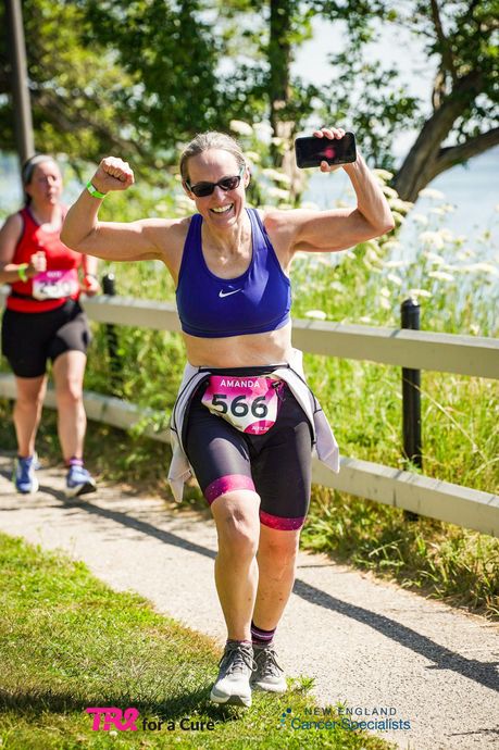Runner in purple top and black leggings raising her arms while jogging on a sunny trail by a white fence
