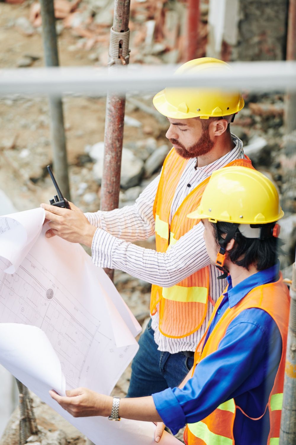 Construction workers in yellow helmets and vests examining blueprints at a construction site.