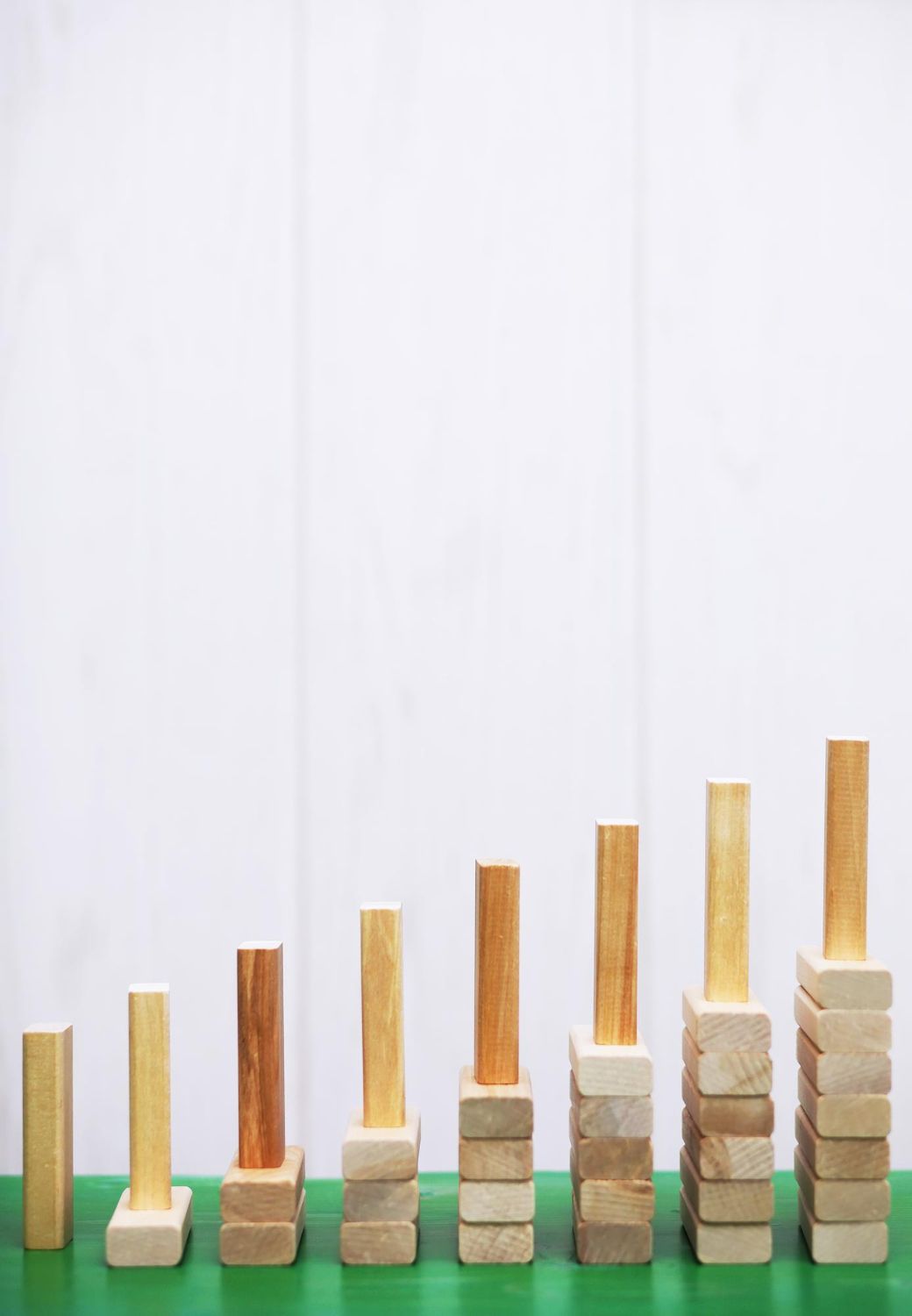 Wooden blocks stacked in ascending order, like a bar graph, on green surface, white background.