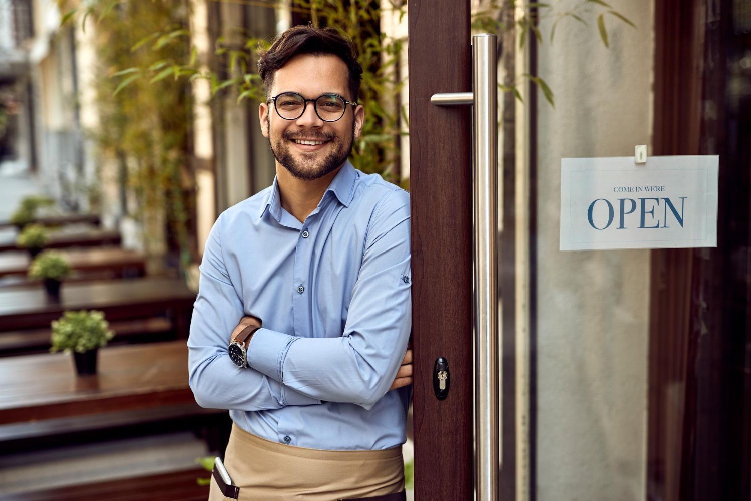 Smiling man, wearing a blue shirt and apron, stands in a doorway with an
