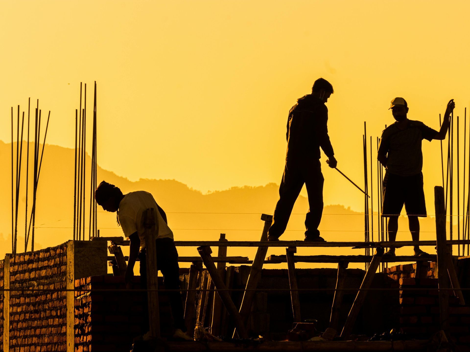 Construction workers silhouetted against a golden sunset, working on a building frame.