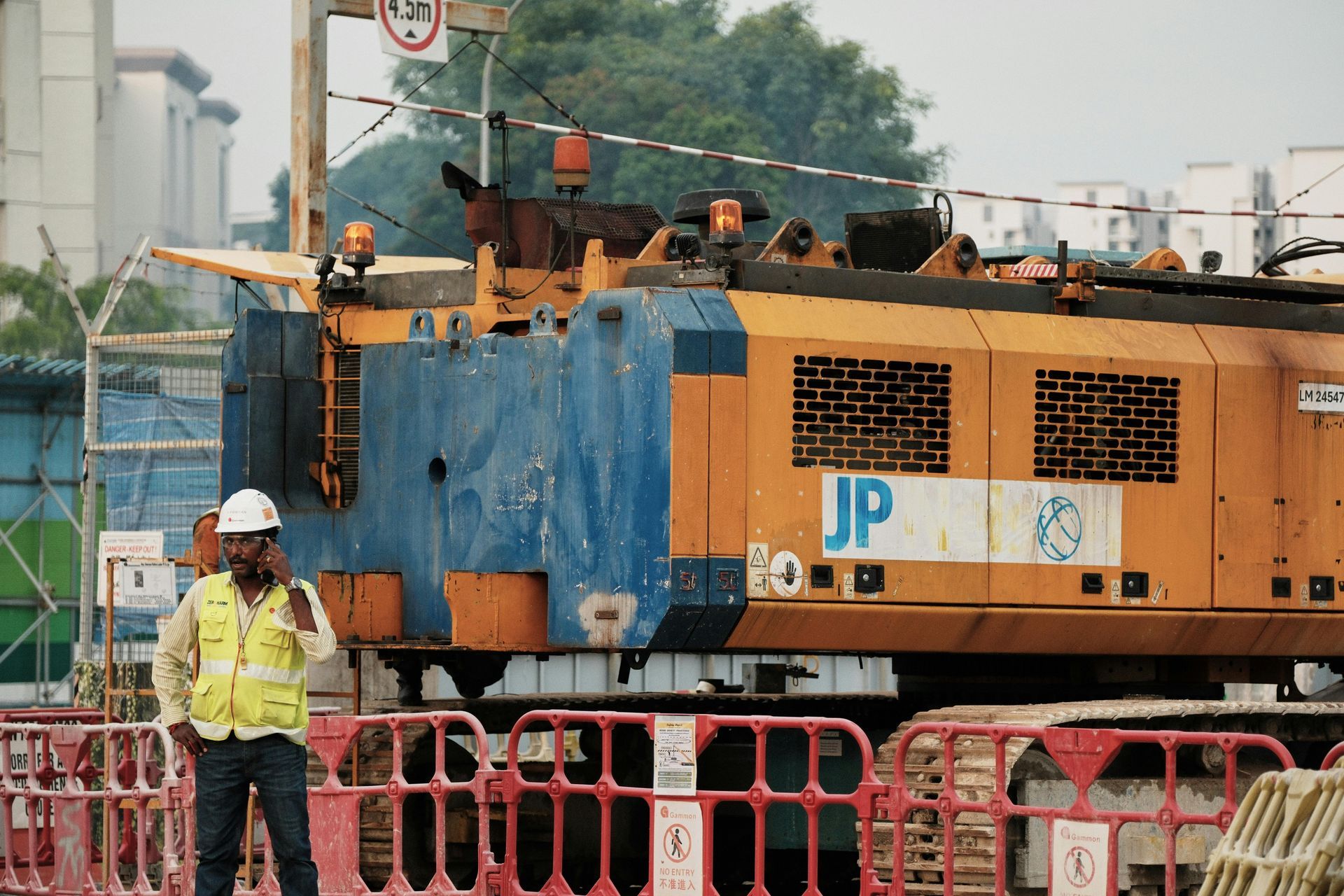 Construction worker near a blue and yellow machine at a construction site with safety barriers.