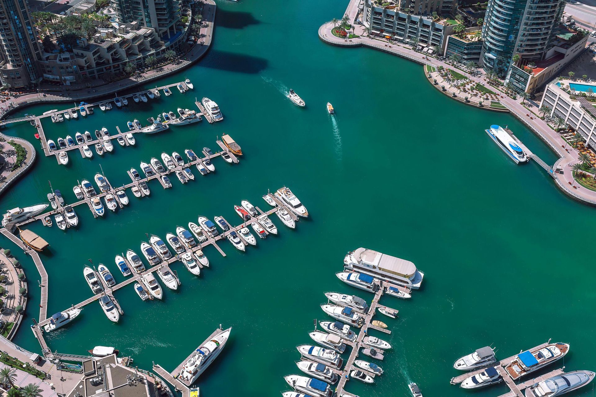 Aerial view of a marina with boats docked, turquoise water, and surrounding buildings.