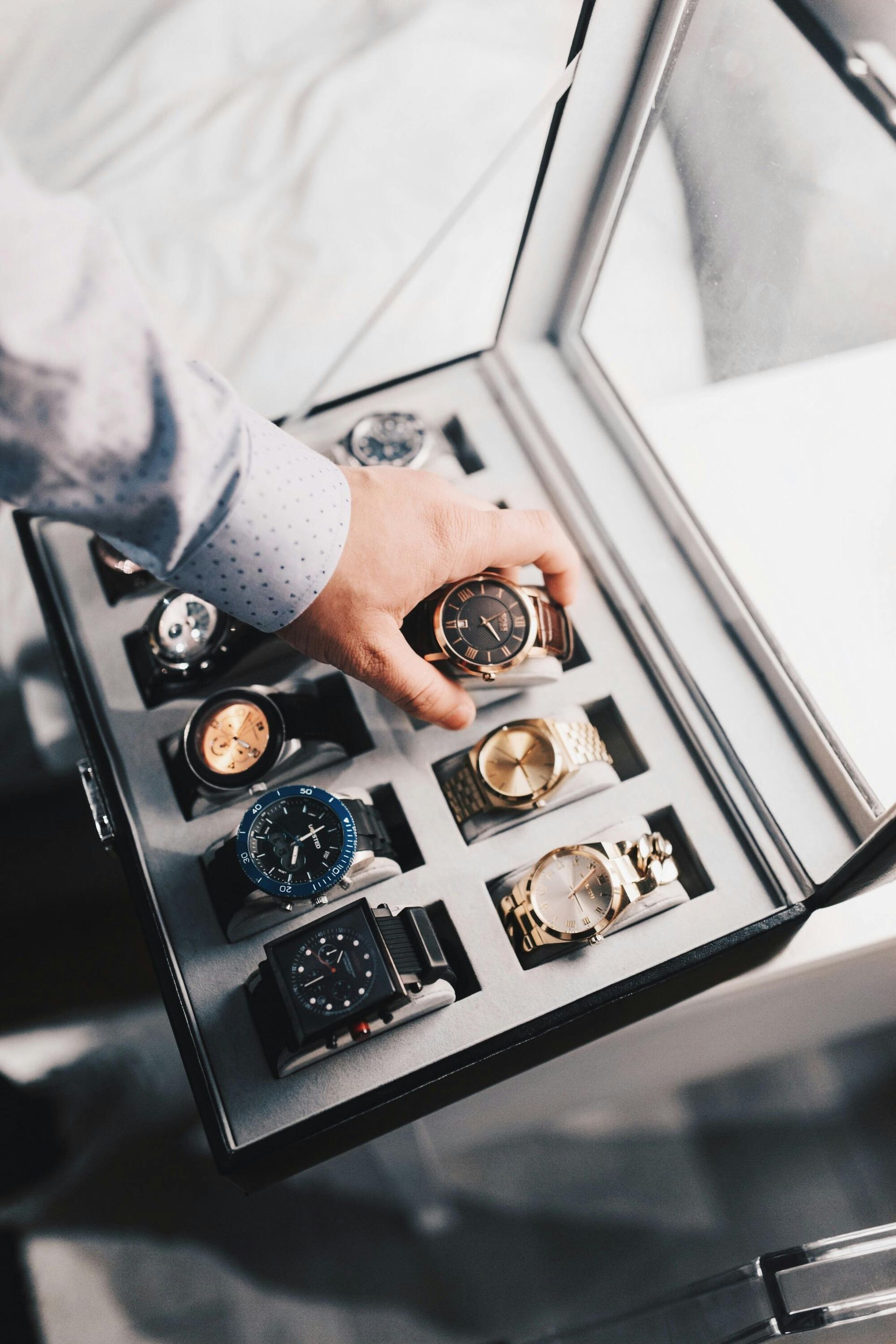 Person selecting a gold watch from a case filled with various luxury watches.