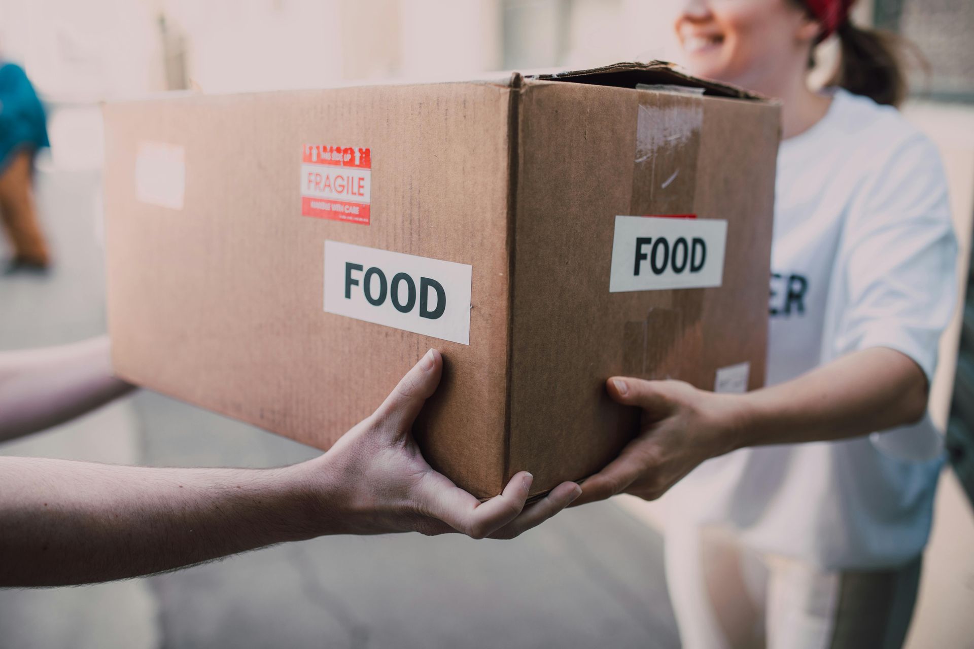 A person handing a cardboard box of food to another person, labeled 