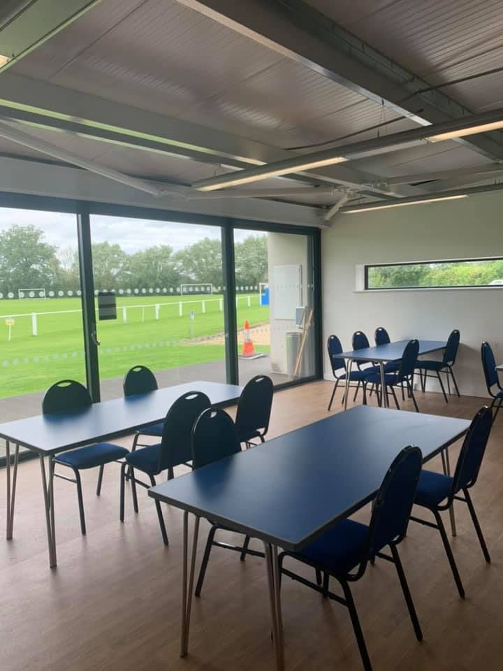 A room at Littlemarsh Pavilion with tables and chairs and a view of a field.