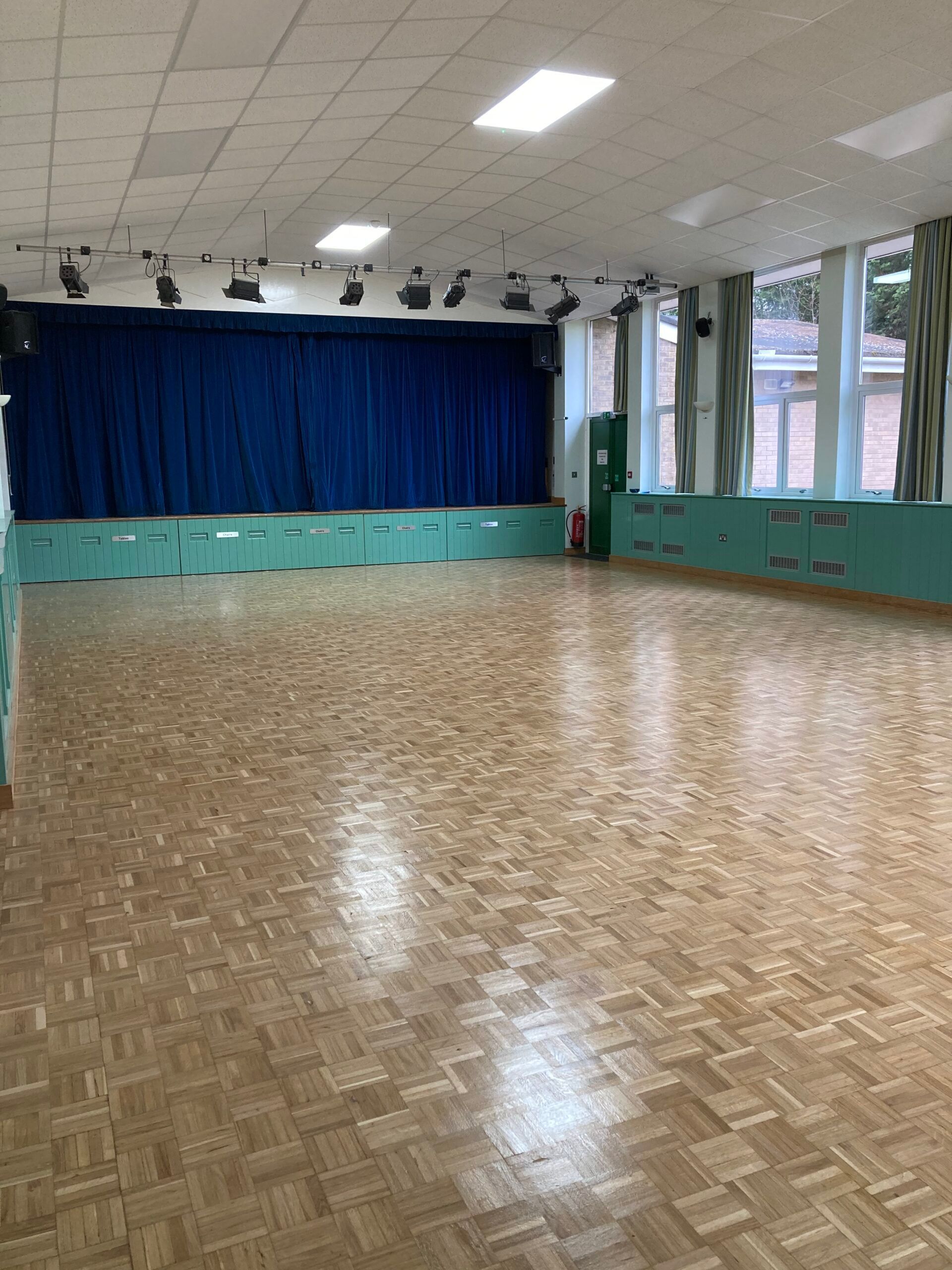 A large empty room with a wooden floor and a blue curtain.