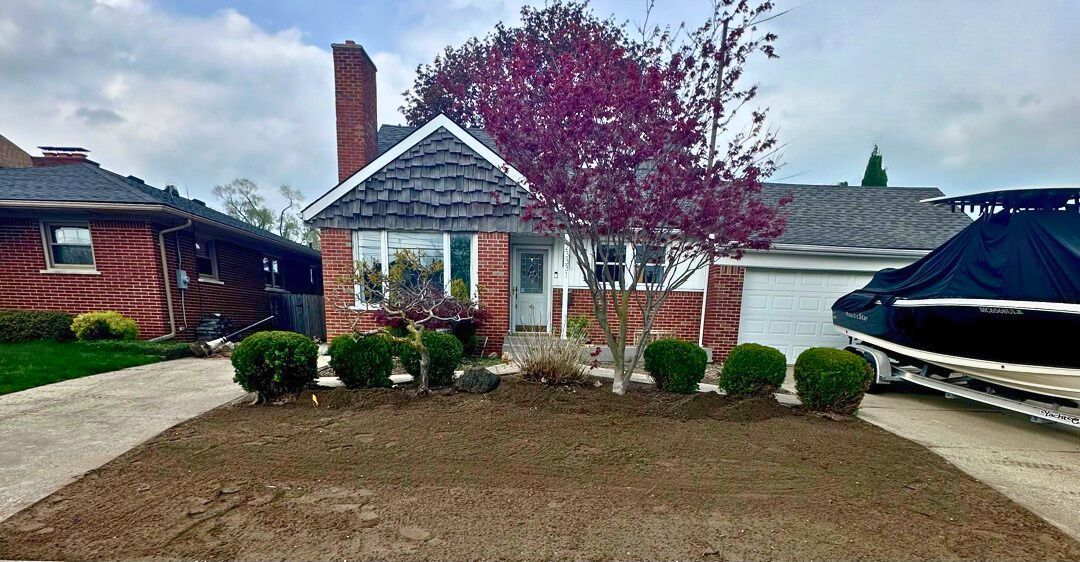 Suburban house with brick chimney, trimmed shrubs, flowering tree, and a driveway on the left