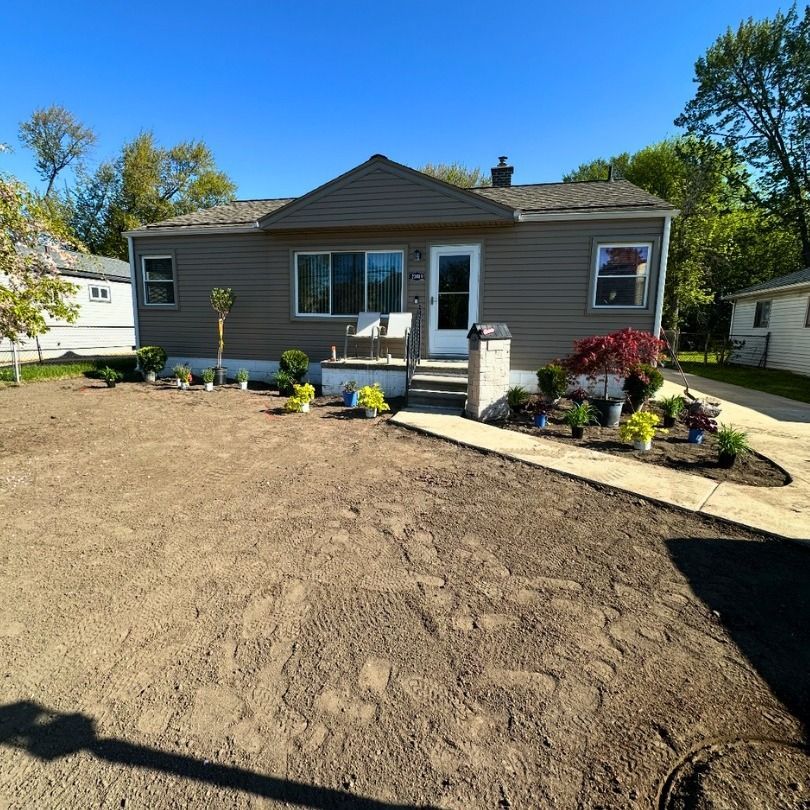 Single-story gray house with a freshly landscaped front yard and bare dirt lawn under a blue sky