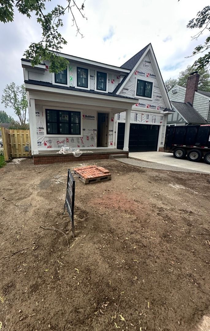 Two-story house under construction with white siding, black trim, and a dirt front yard