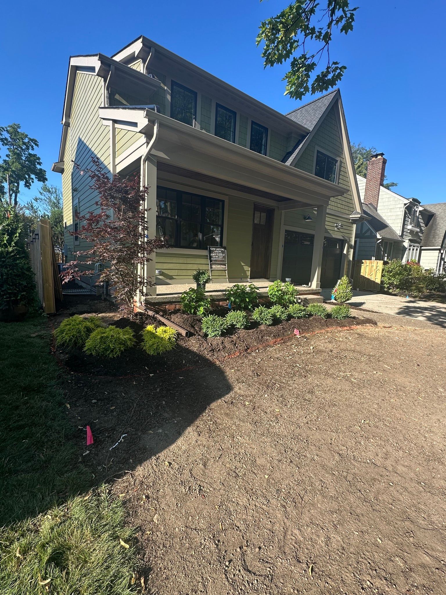 Front porch of a beige house with dark trim, front steps, and a mulched yard in bright sunlight