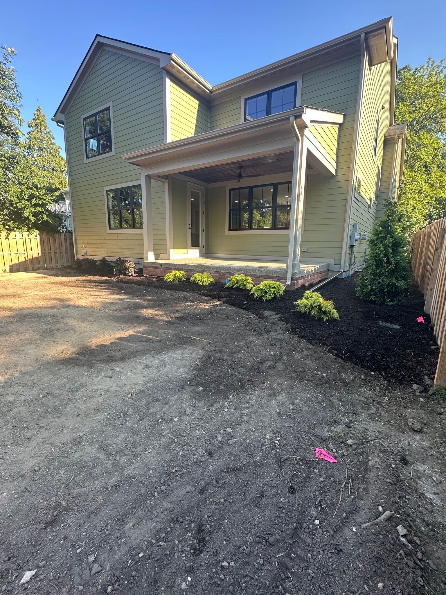 Two-story beige house with a front porch and gravel driveway in bright daylight.