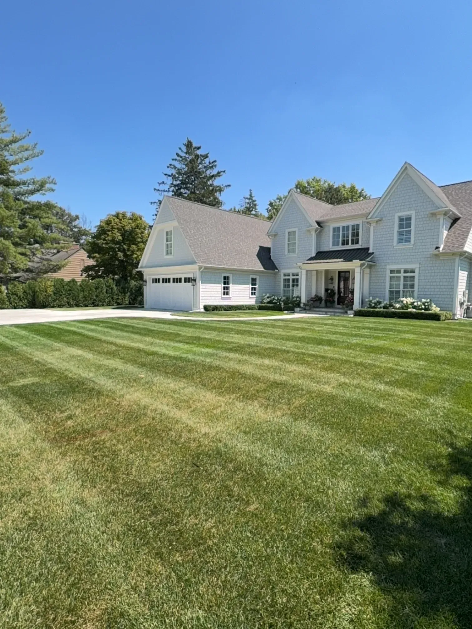 Sunny suburban house with a curved sidewalk, green lawn, and leafless trees beside a driveway