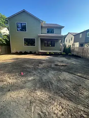 Backyard view of a beige two-story house with a dirt lot and wooden fence on both sides
