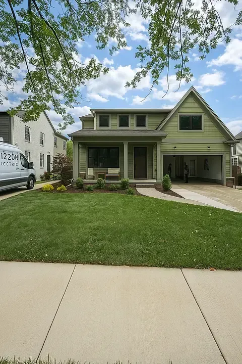 Green two-story suburban house with a front porch, driveway, and trimmed lawn under a partly cloudy sky