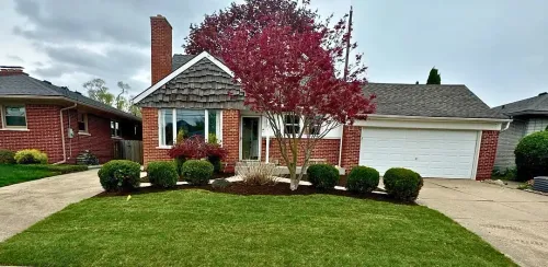 Suburban brick house with white garage, red tree in front, and a neatly trimmed green lawn