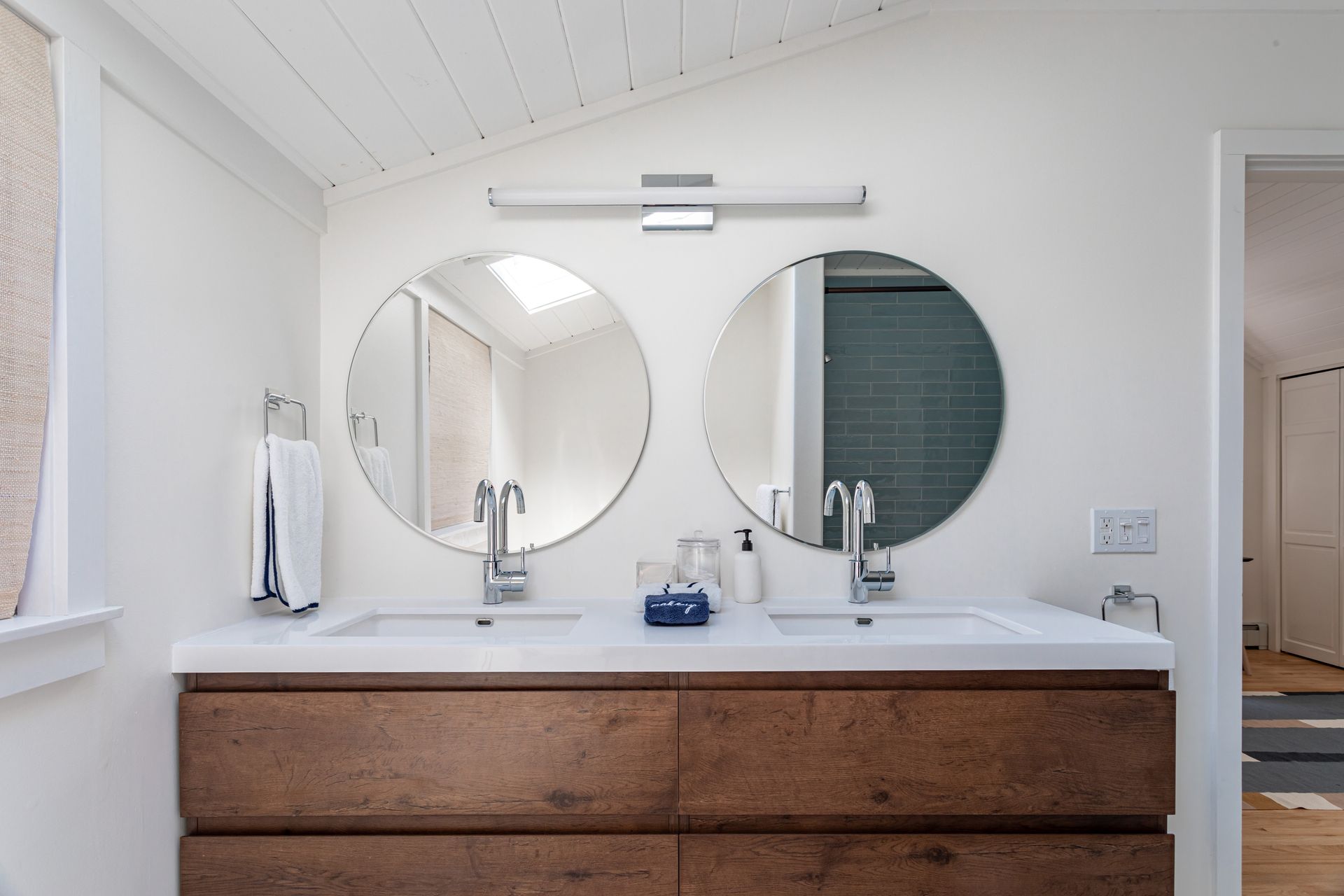 A bathroom vanity with two round mirrors above a double sink and wooden cabinet.