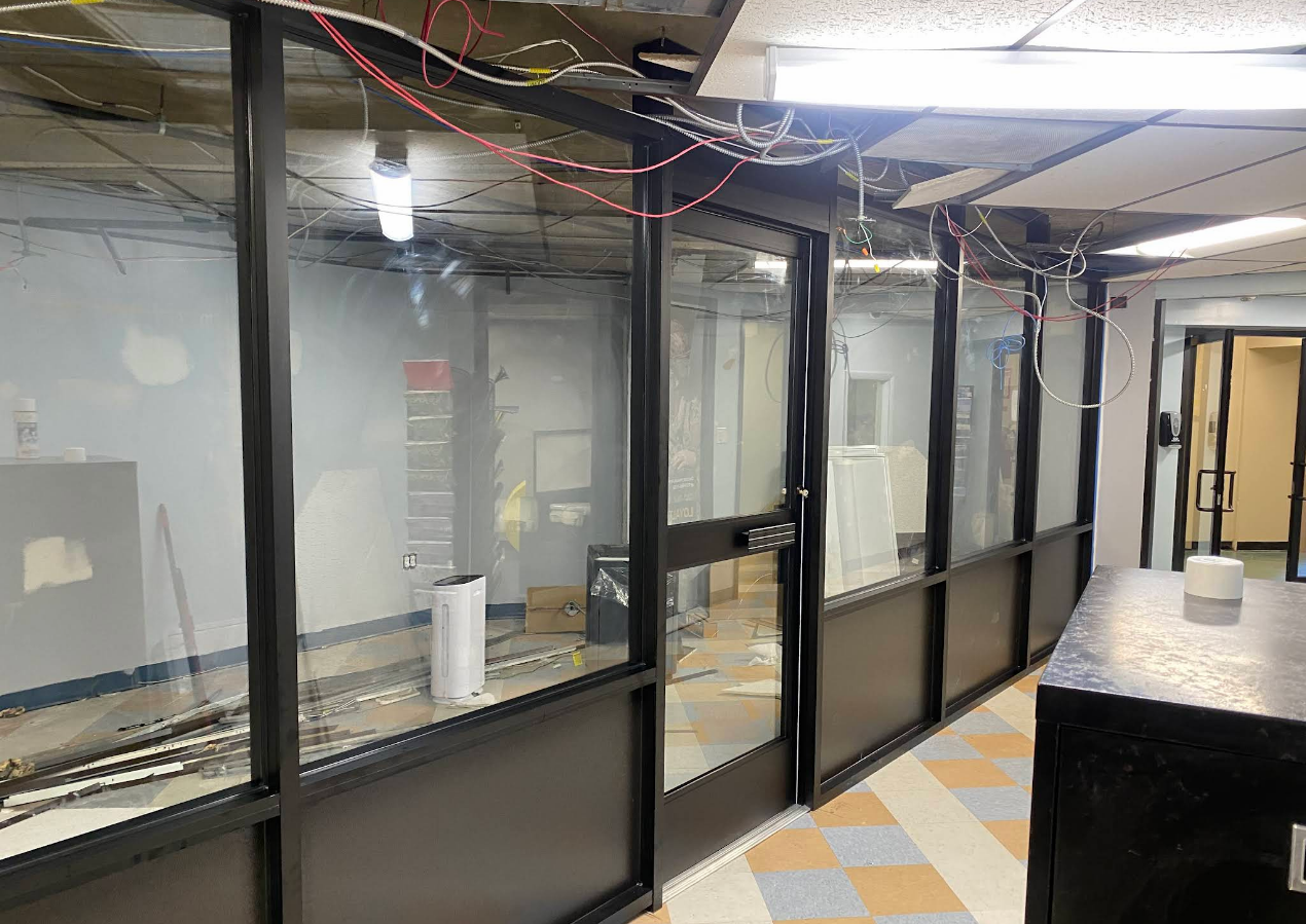 Glass-walled room with a door, wires overhead. Black frames with white and blue tiled floor.