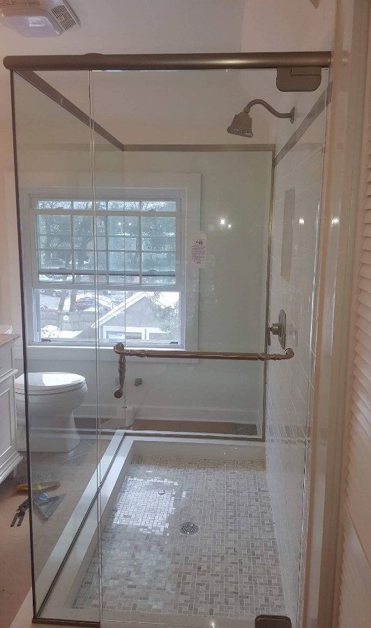 Glass shower enclosure in a bathroom with window, toilet, and patterned tile.