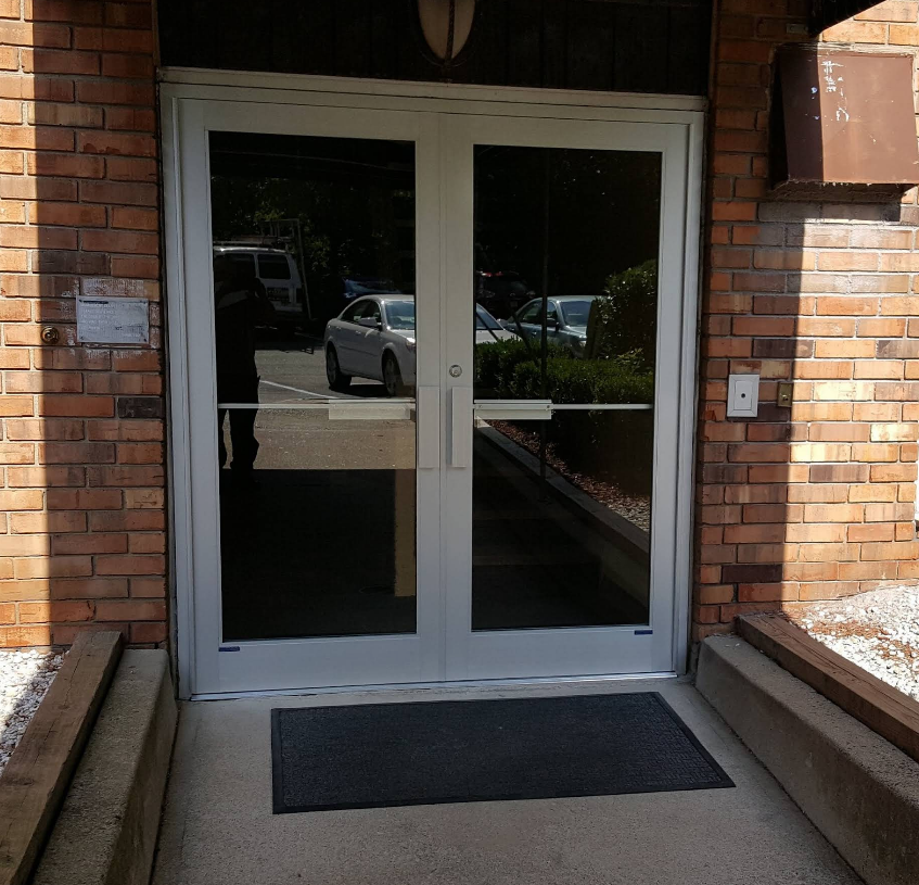 Double glass doors with push bar and mat, set in brick building entrance.