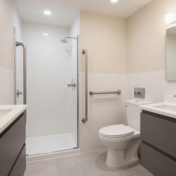 Baño moderno y accesible con ducha a ras de suelo, inodoro y lavabo en acabados blancos y grises.