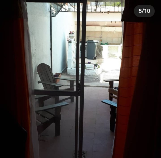Vista a través de una puerta hacia un pequeño patio con sillas, una mesa y un cubo de basura a plena luz del día.