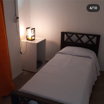 Habitación pequeña con una cama individual, ropa de cama blanca y una lámpara de noche encendida.