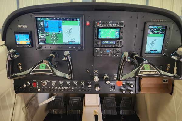 Aircraft cockpit with dual control yokes and illuminated flight displays inside a small plane.