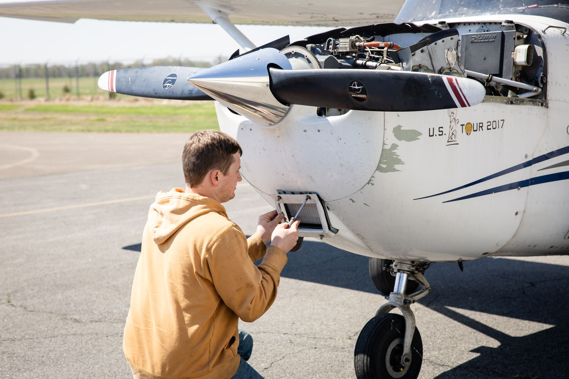 Person inspecting the nose of a small white airplane on a sunny runway