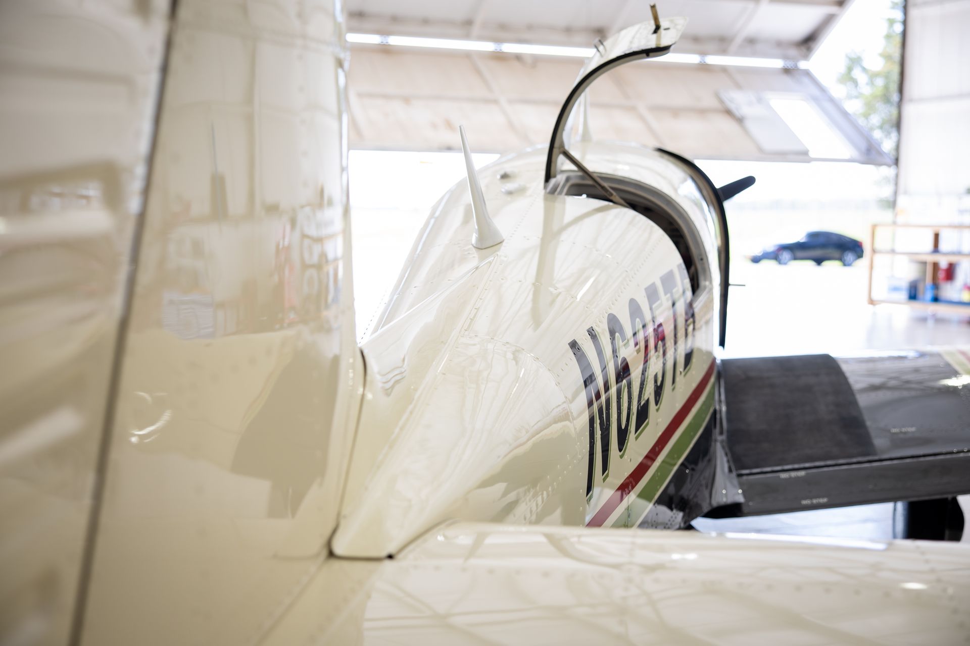Small white airplane with red and green stripe in a hangar, viewed from the side.