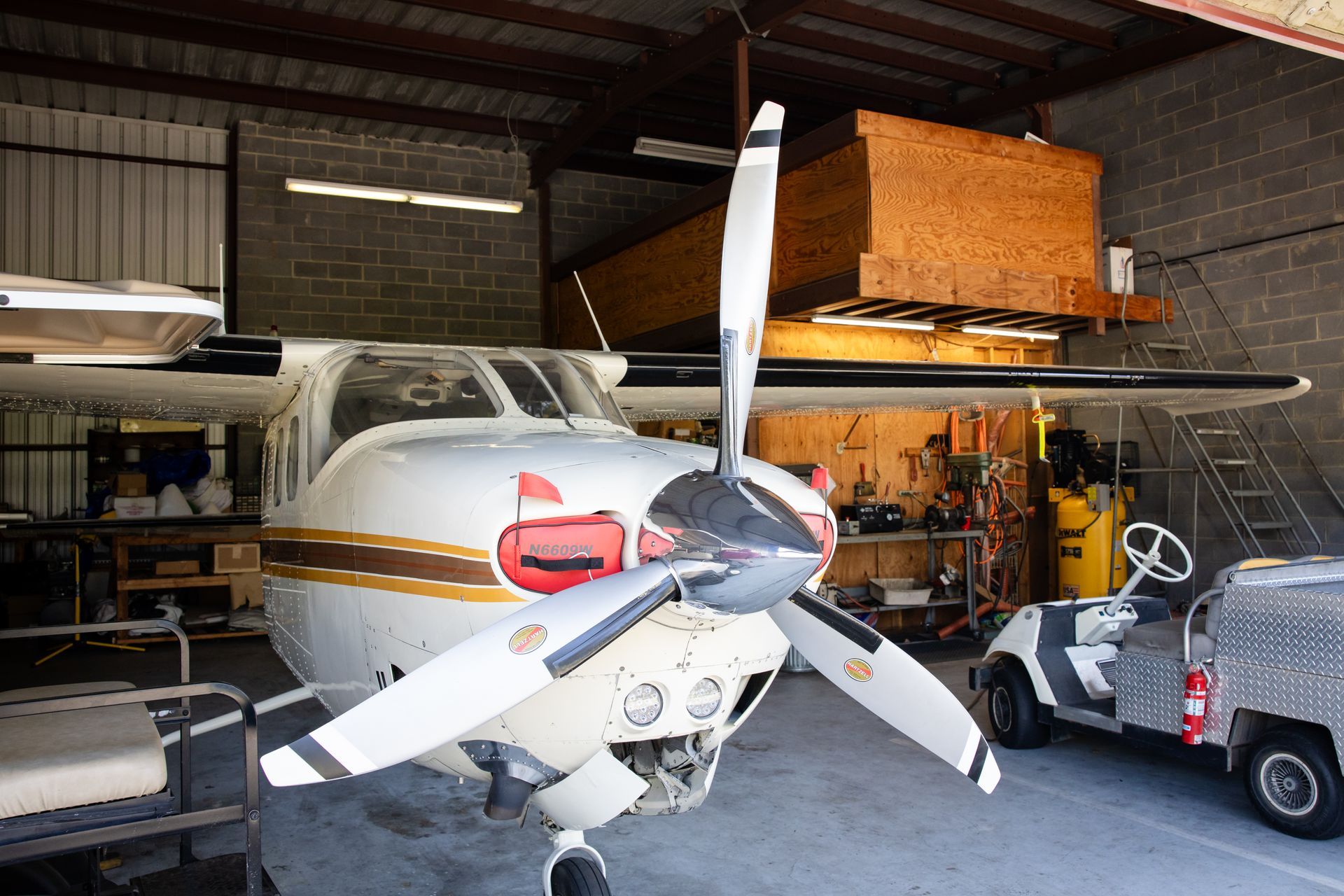 Small airplane in a hangar with front propeller, tools, and a golf cart nearby