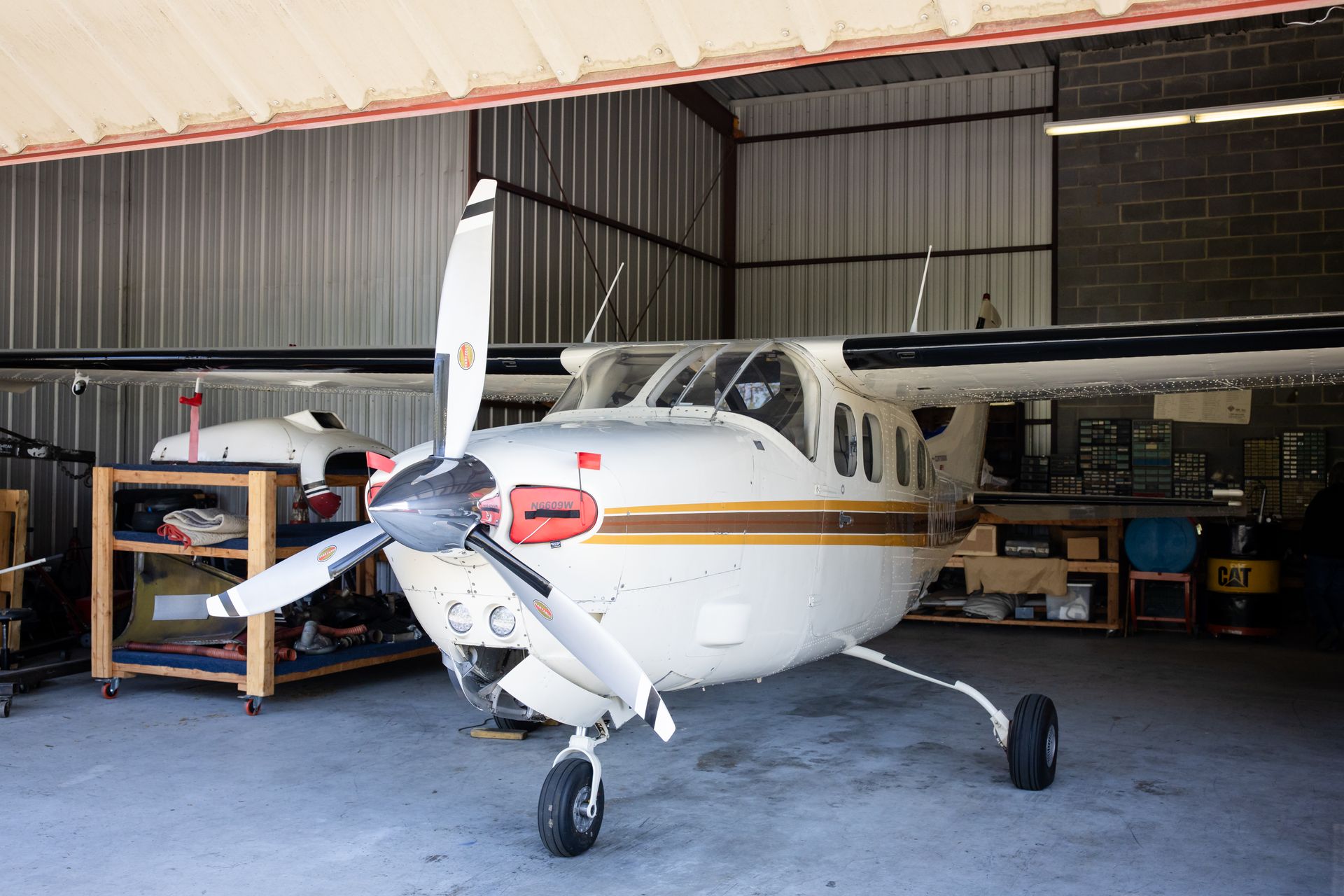 Small white airplane in a hangar with maintenance tools and equipment nearby