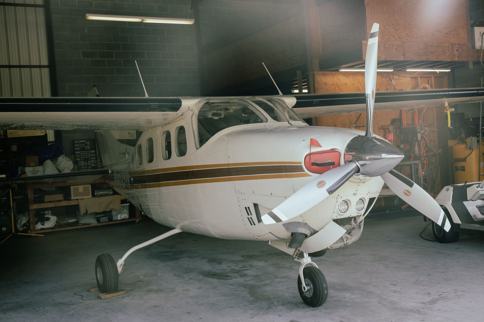 White single-engine airplane parked in a hangar, front view with red nose and wing stripes