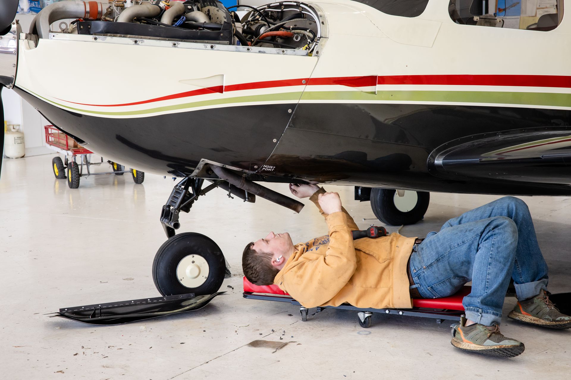 Mechanic working beneath a small airplane on a creeper in a hangar