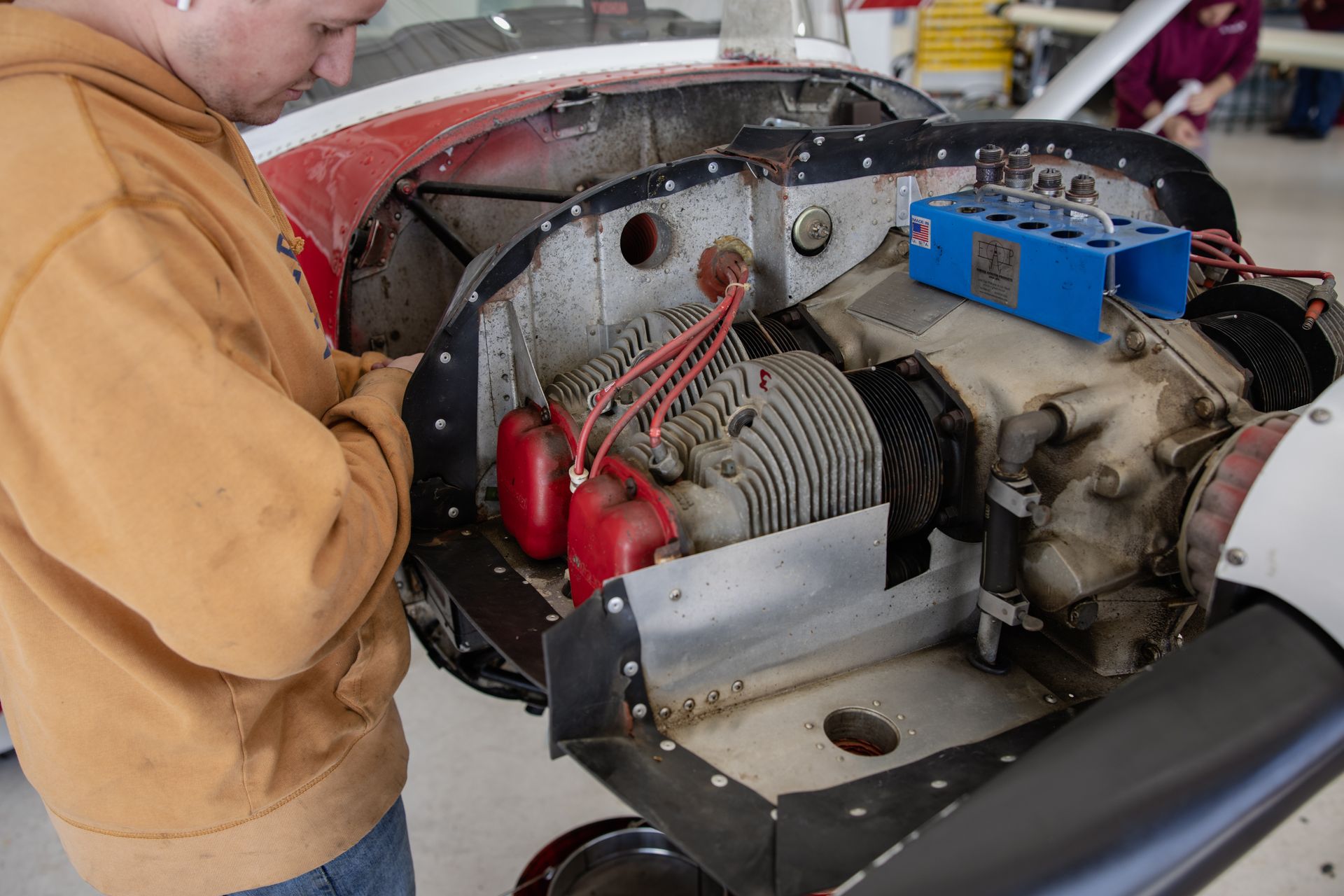 Man inspecting a small aircraft engine compartment with red and silver components in a garage