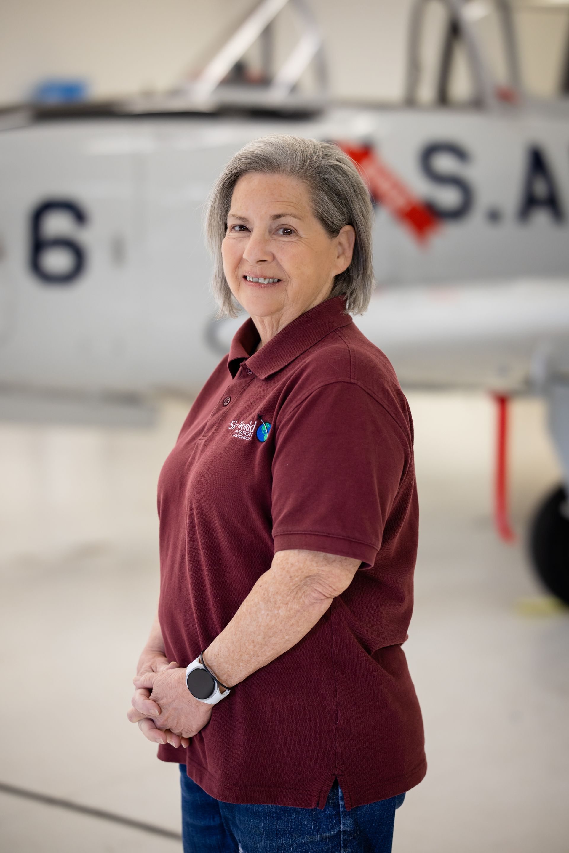 Woman in maroon polo standing in front of an aircraft inside a hangar