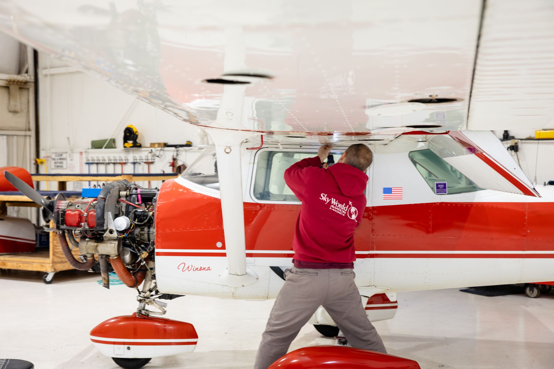 Red and white fuel drum under an aircraft engine in a hangar, with hoses and tools nearby