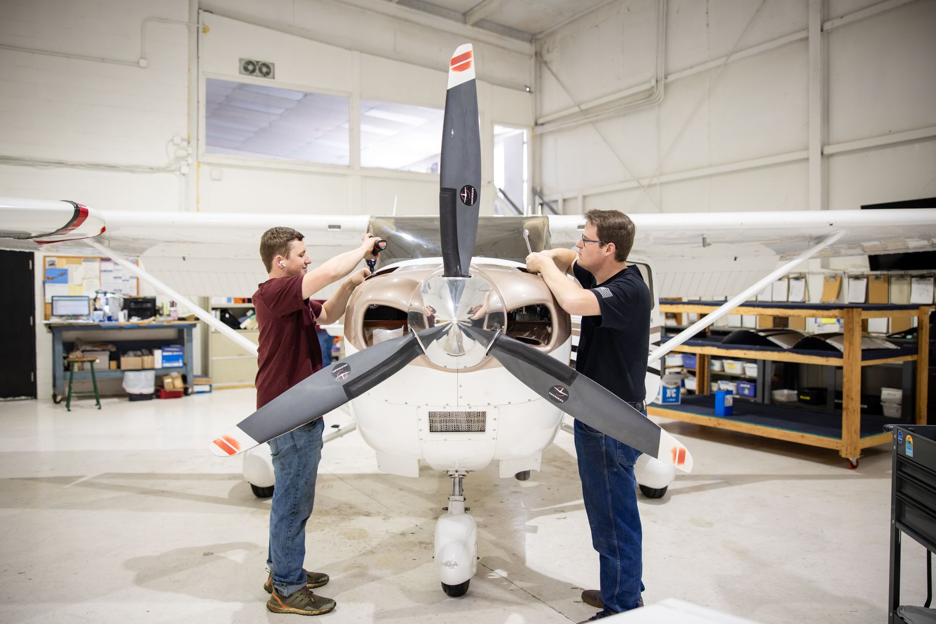 Red and white airplane in a hangar with a person inspecting the exposed engine.