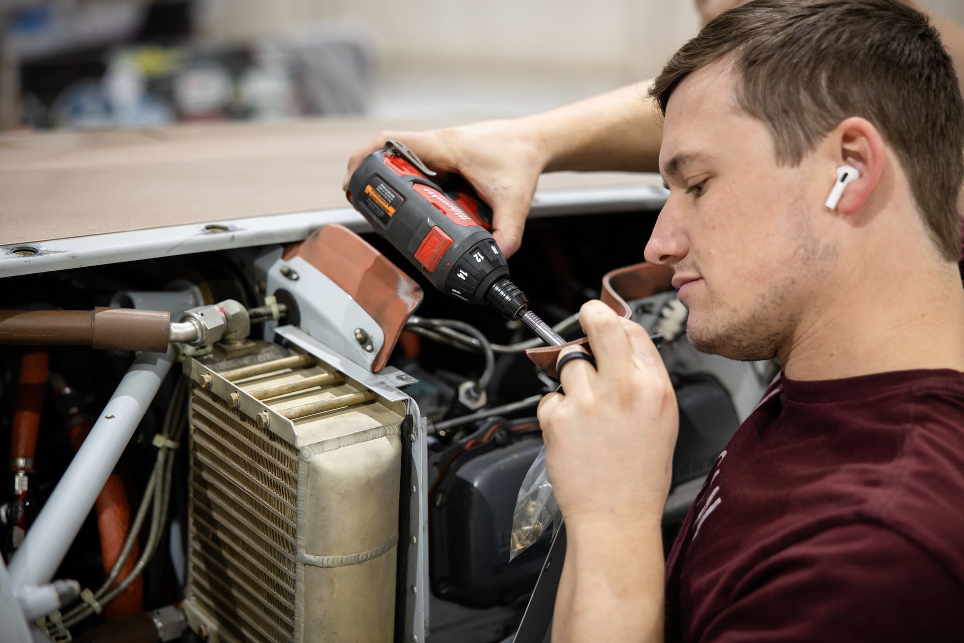 Person in a maroon shirt working on a small aircraft in a hangar