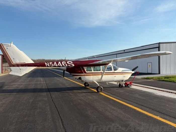 Small red-and-white prop plane parked on a runway beside a hangar under a blue sky