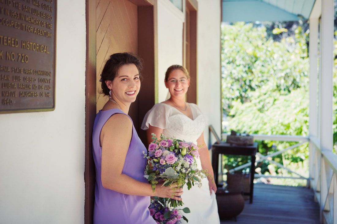 A bride and her bridesmaid are posing for a picture on a porch.