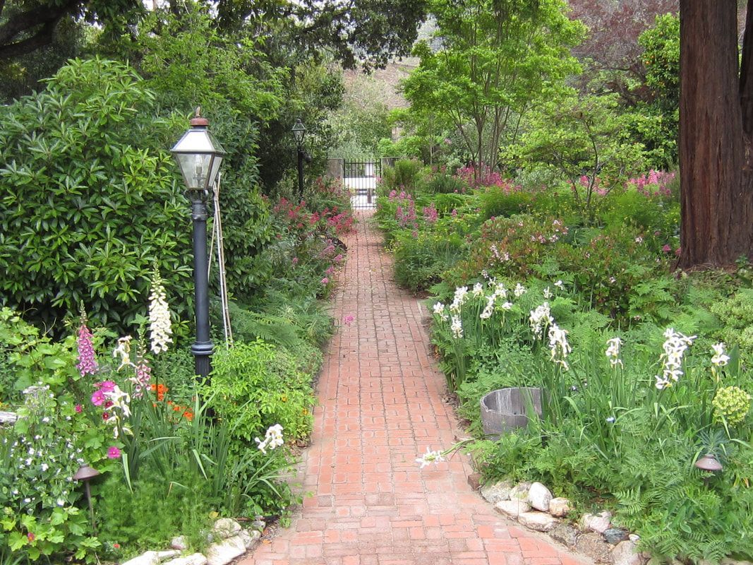 A brick walkway surrounded by flowers and trees in a garden.