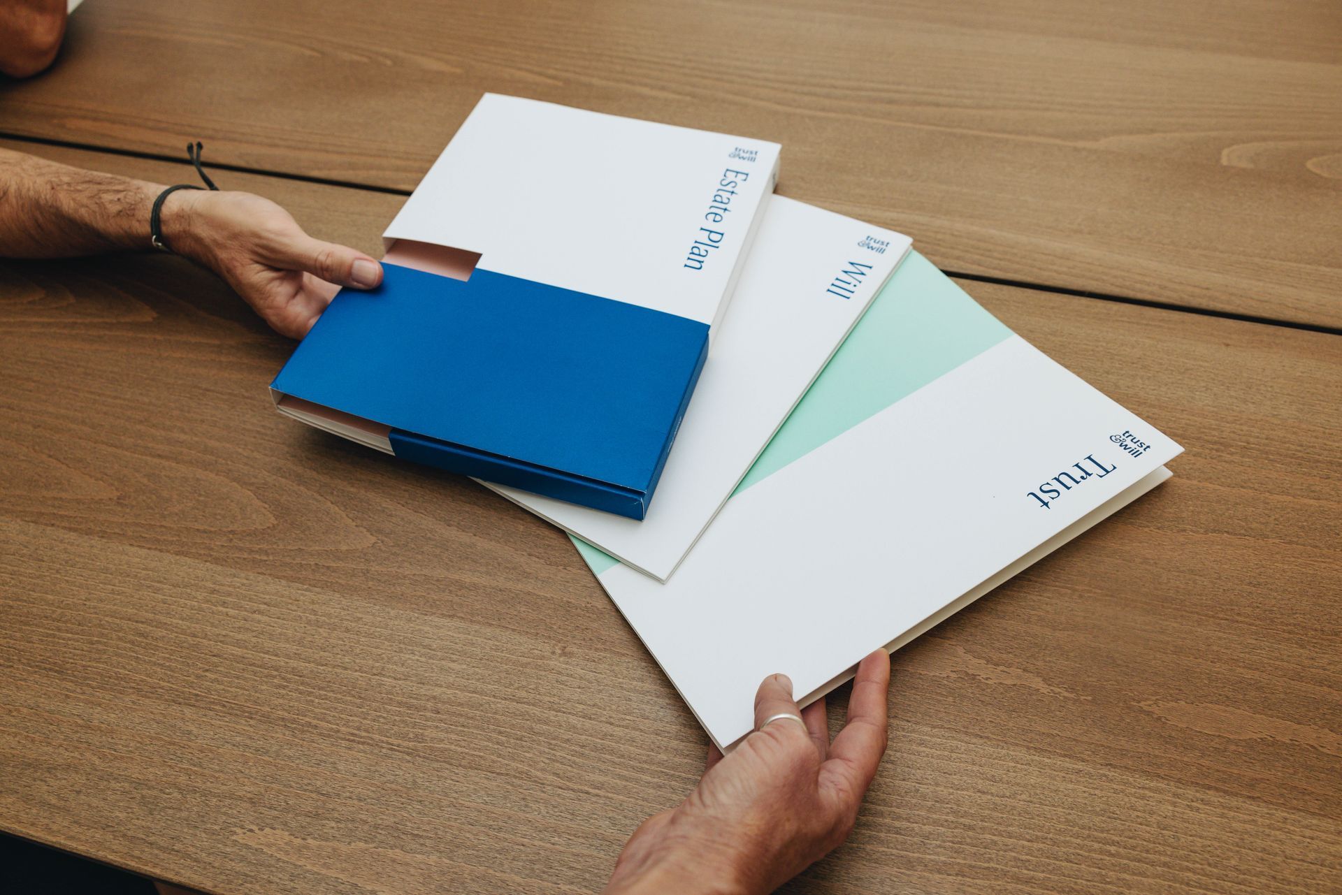 A person is holding a stack of folders on a wooden table.