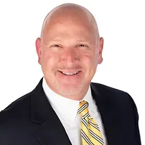 A bald man in a suit and tie is smiling for the camera.